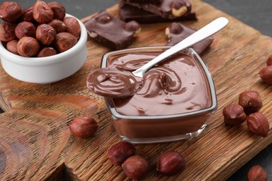 Photo of Bowl with tasty paste, chocolate pieces and nuts on wooden board, closeup