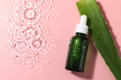 Photo of Bottle of cosmetic product and aloe leaf in water on pink background, flat lay. Space for text