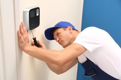 Male technician installing security alarm system indoors