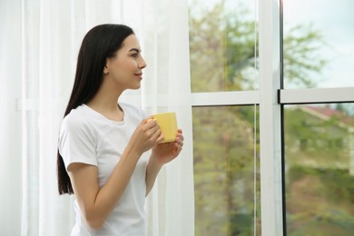 Photo of Young woman with cup of drink relaxing near window home, space for text