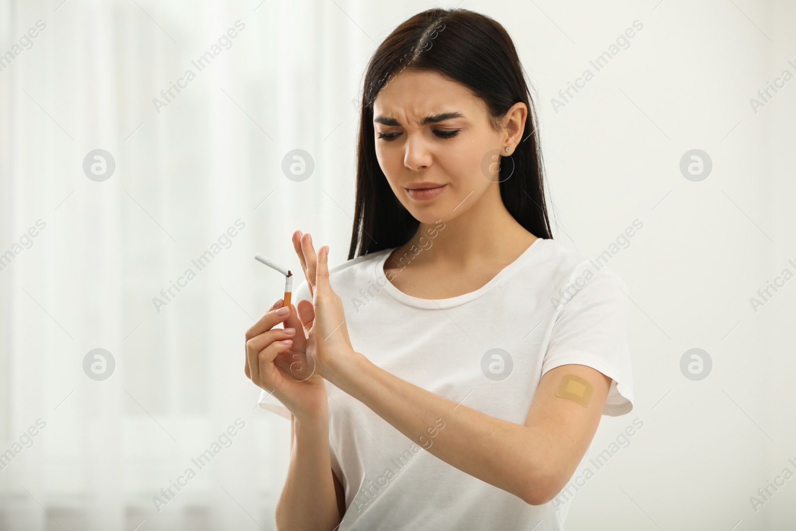 Photo of Emotional young woman with nicotine patch and cigarette at home