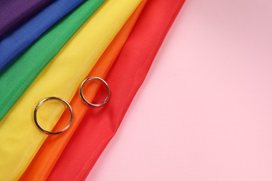 Photo of Rainbow LGBT flag and wedding rings on pink background, top view. Space for text