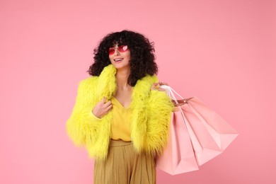 Happy young woman with shopping bags on pink background