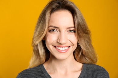 Photo of Portrait of happy young woman with beautiful blonde hair and charming smile on yellow background, closeup