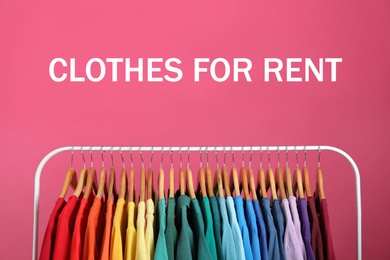Rack with bright clothes for rent on pink background