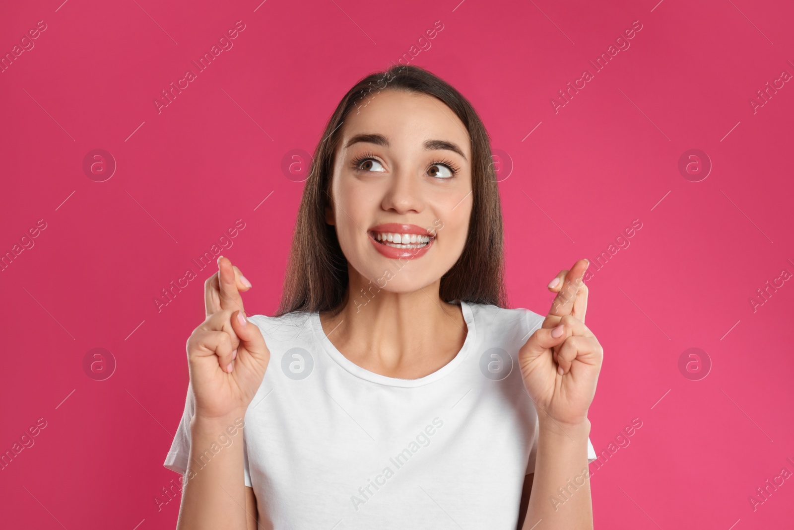 Photo of Woman with crossed fingers on pink background. Superstition concept