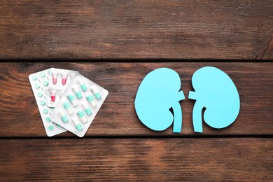 Photo of Paper cutout of kidneys and pills on wooden table, flat lay