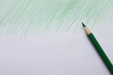 Photo of Green pencil on sheet of paper with drawing, top view. Space for text