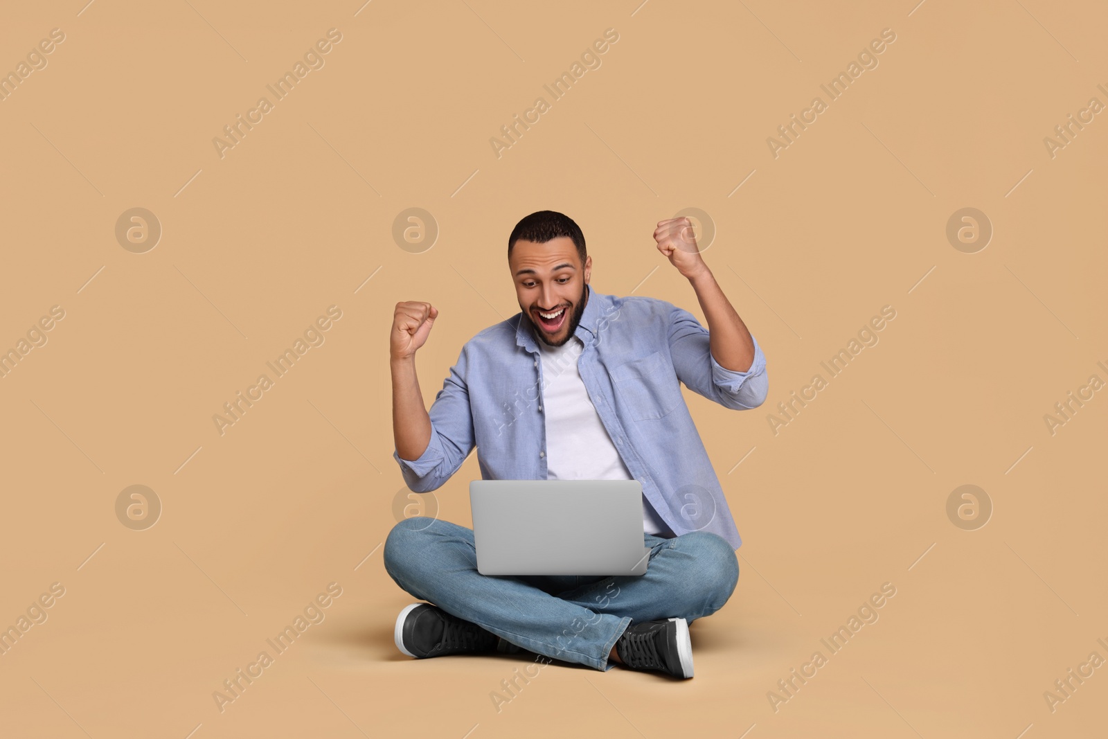 Photo of Happy young man with laptop on beige background