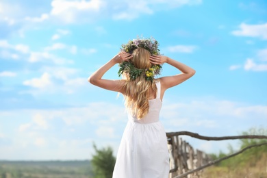 Young woman wearing wreath made of beautiful flowers outdoors on sunny day, back view