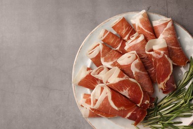 Photo of Rolled slices of delicious jamon with rosemary on grey table, top view. Space for text