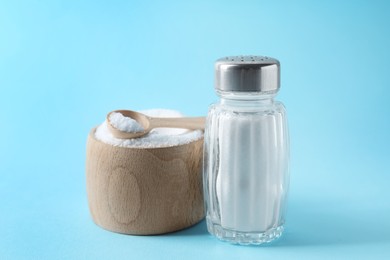 Photo of Organic white salt in bowl and shaker on light blue background, closeup