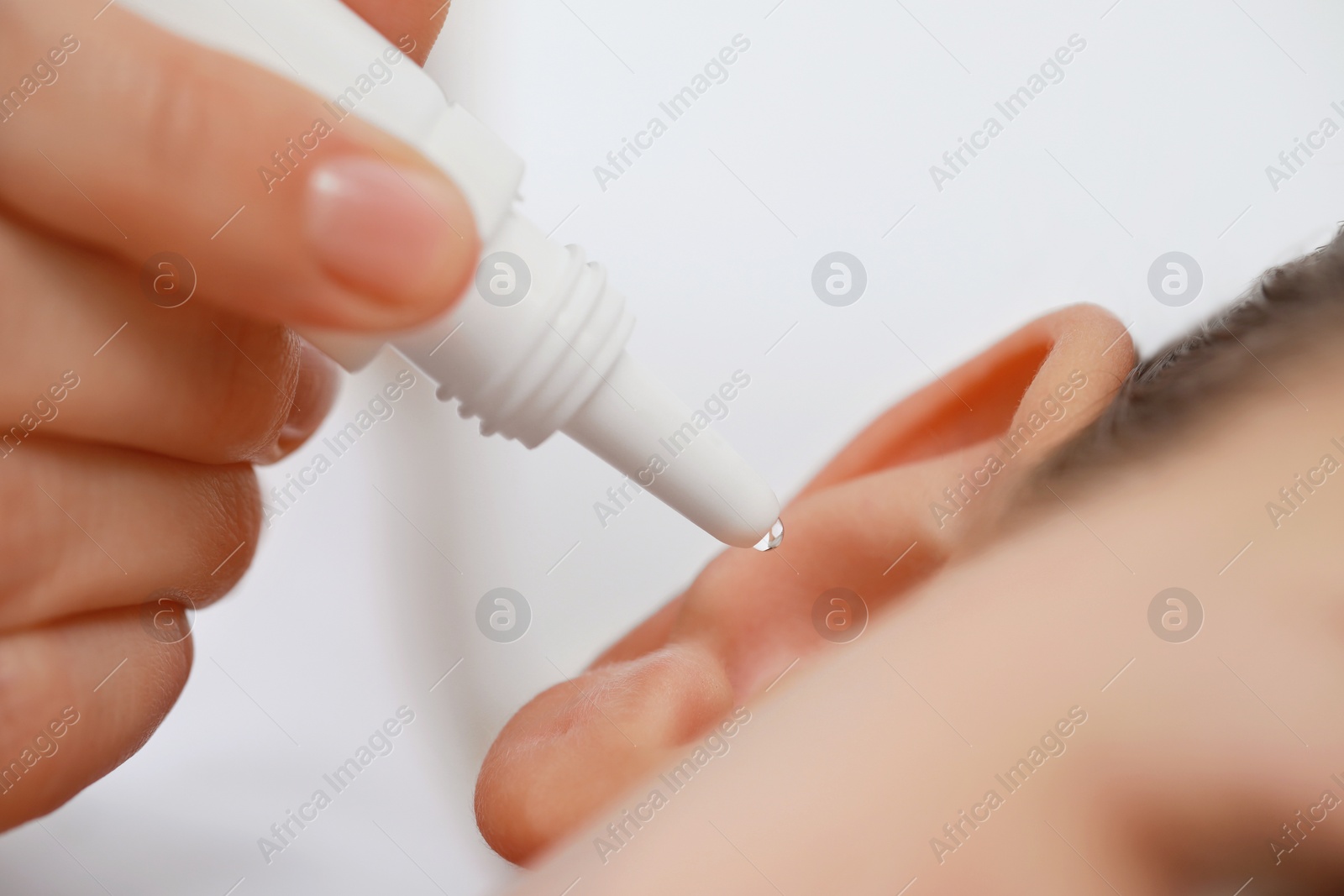 Photo of Mother dripping medication into daughter's ear on light background, closeup