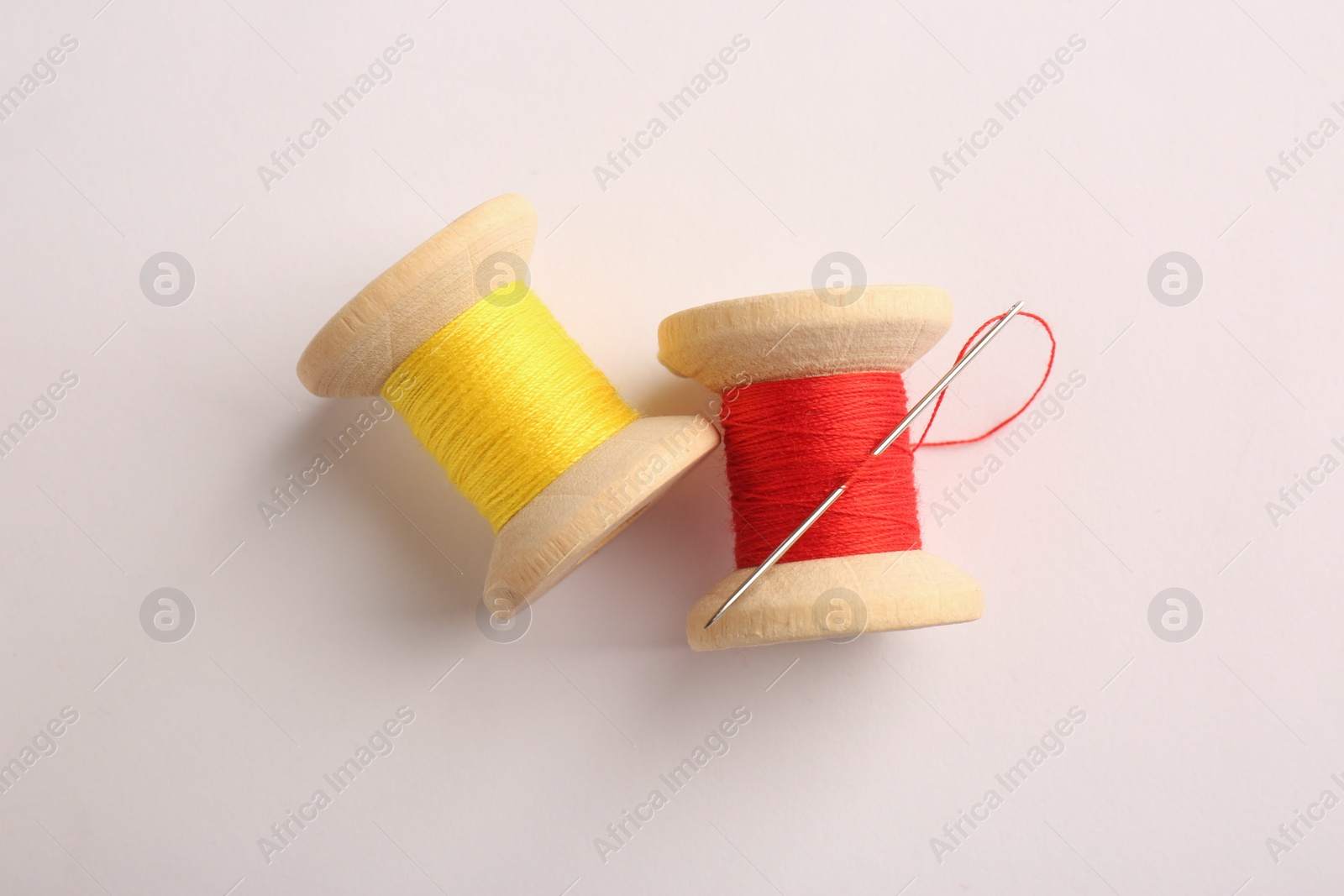 Photo of Colorful sewing threads with needle on light background, flat lay