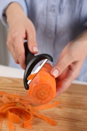 Photo of Woman peeling fresh carrot at table indoors, closeup