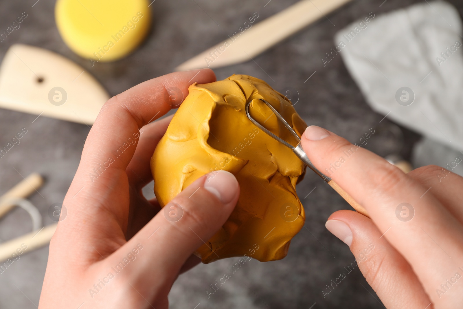 Photo of Woman working with ribbon tool and clay at grey stone table, closeup