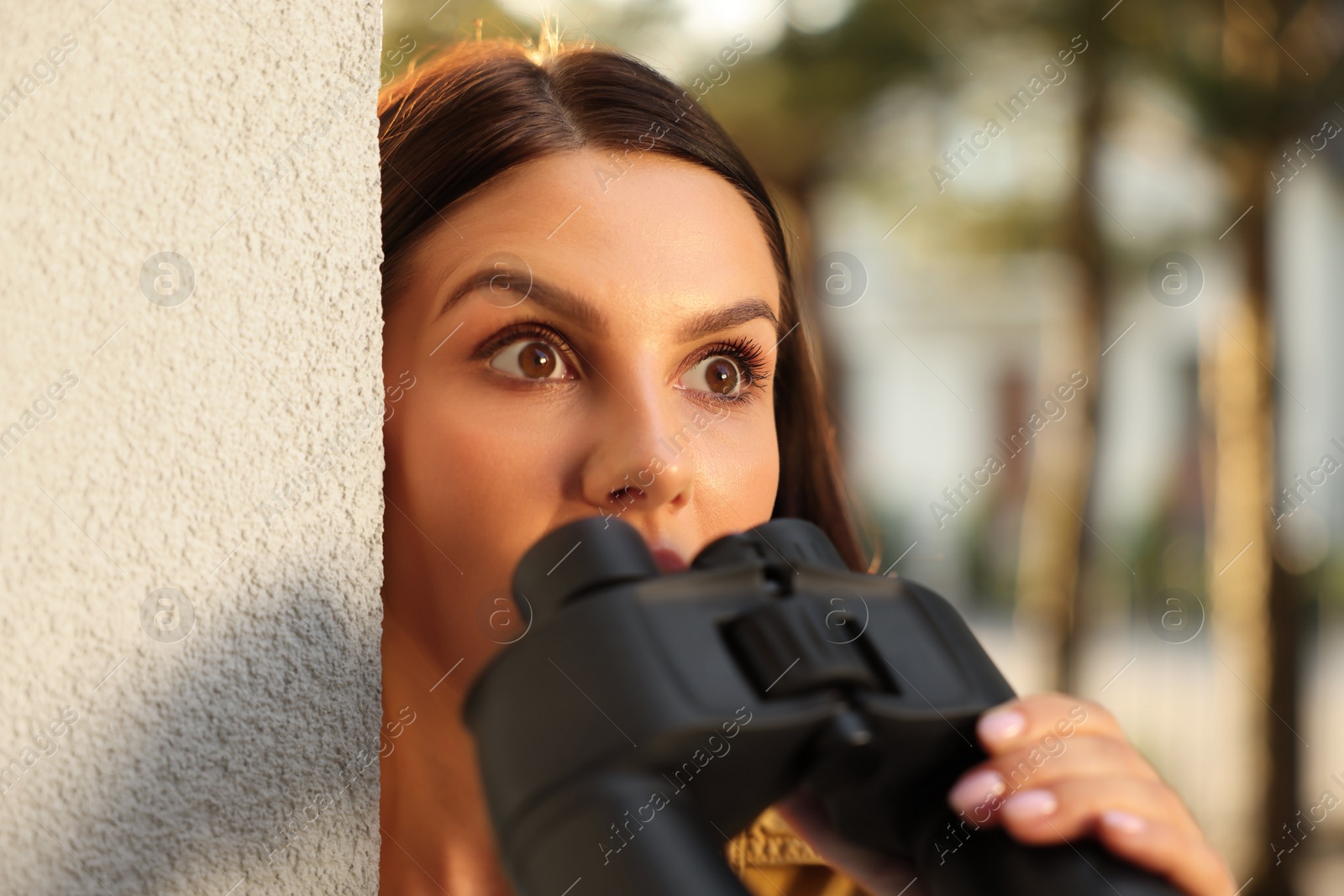 Photo of Concept of private life. Curious young woman with binoculars spying on neighbours outdoors, closeup