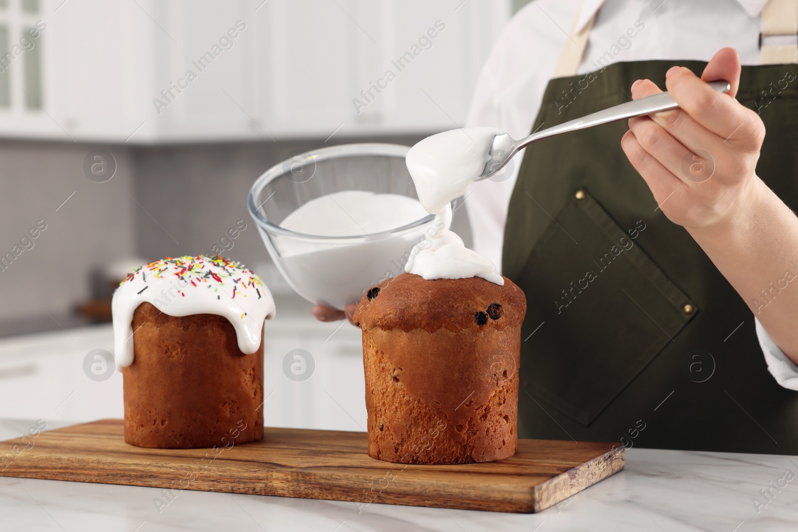 Photo of Woman decorating traditional Easter cake with glaze at white marble table in kitchen, closeup