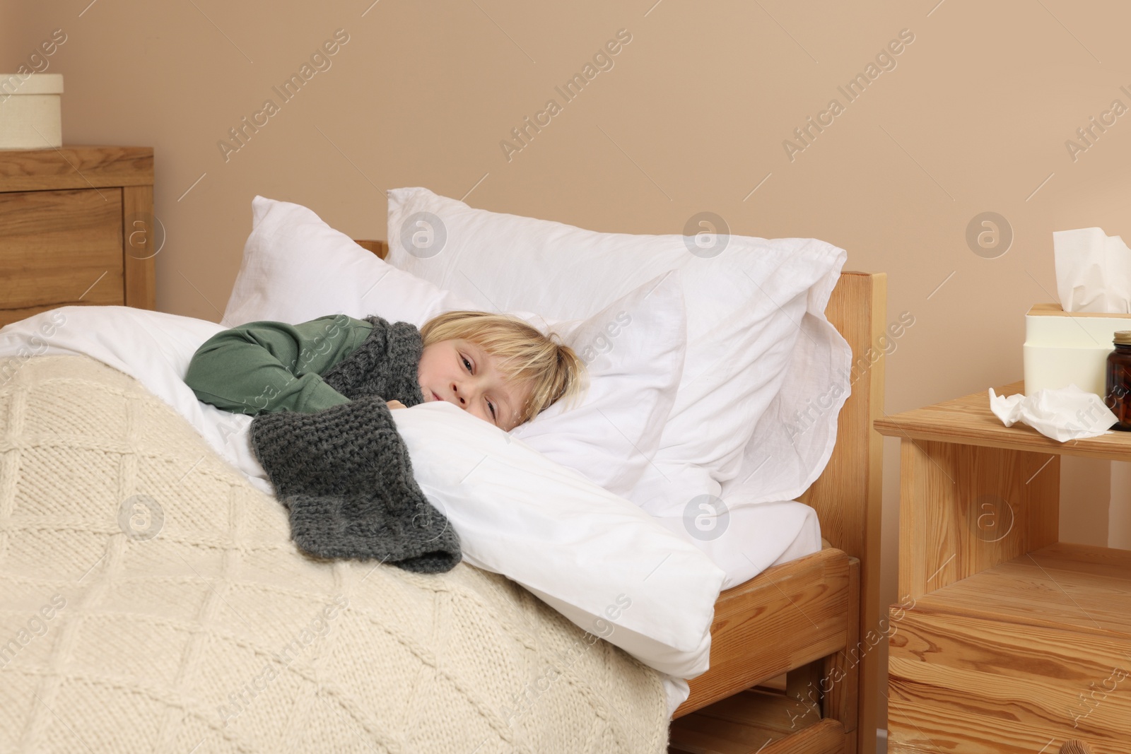 Photo of Sick boy with scarf around neck lying in bed at home