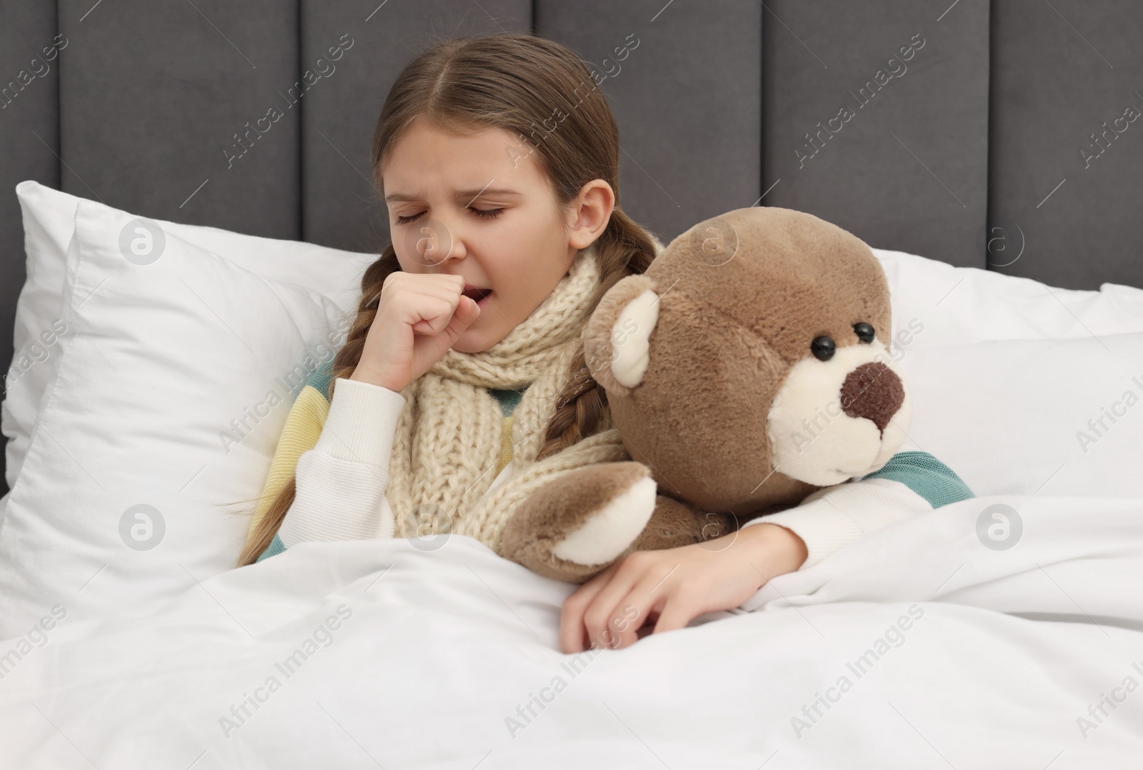 Photo of Sick girl with teddy bear coughing on bed at home