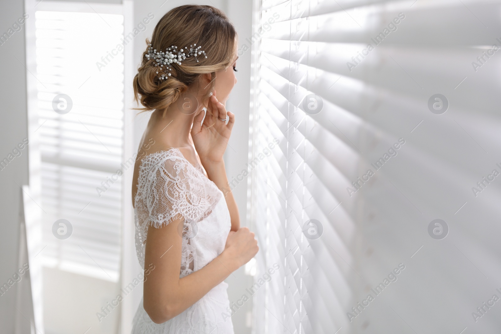 Photo of Young bride with elegant wedding hairstyle near window indoors