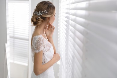 Young bride with elegant wedding hairstyle near window indoors