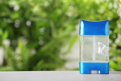 Photo of Deodorant container on white wooden table against blurred background. Space for text