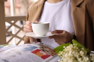Woman with cup of coffee reading magazine at outdoor cafe in morning, closeup