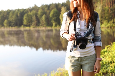 Young female photographer with camera on shore of lake. Camping season