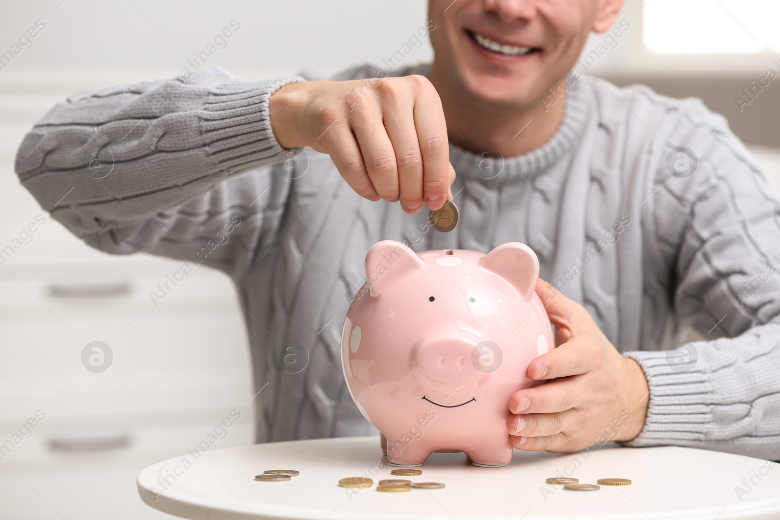 Photo of Man putting coin into piggy bank at white table, closeup