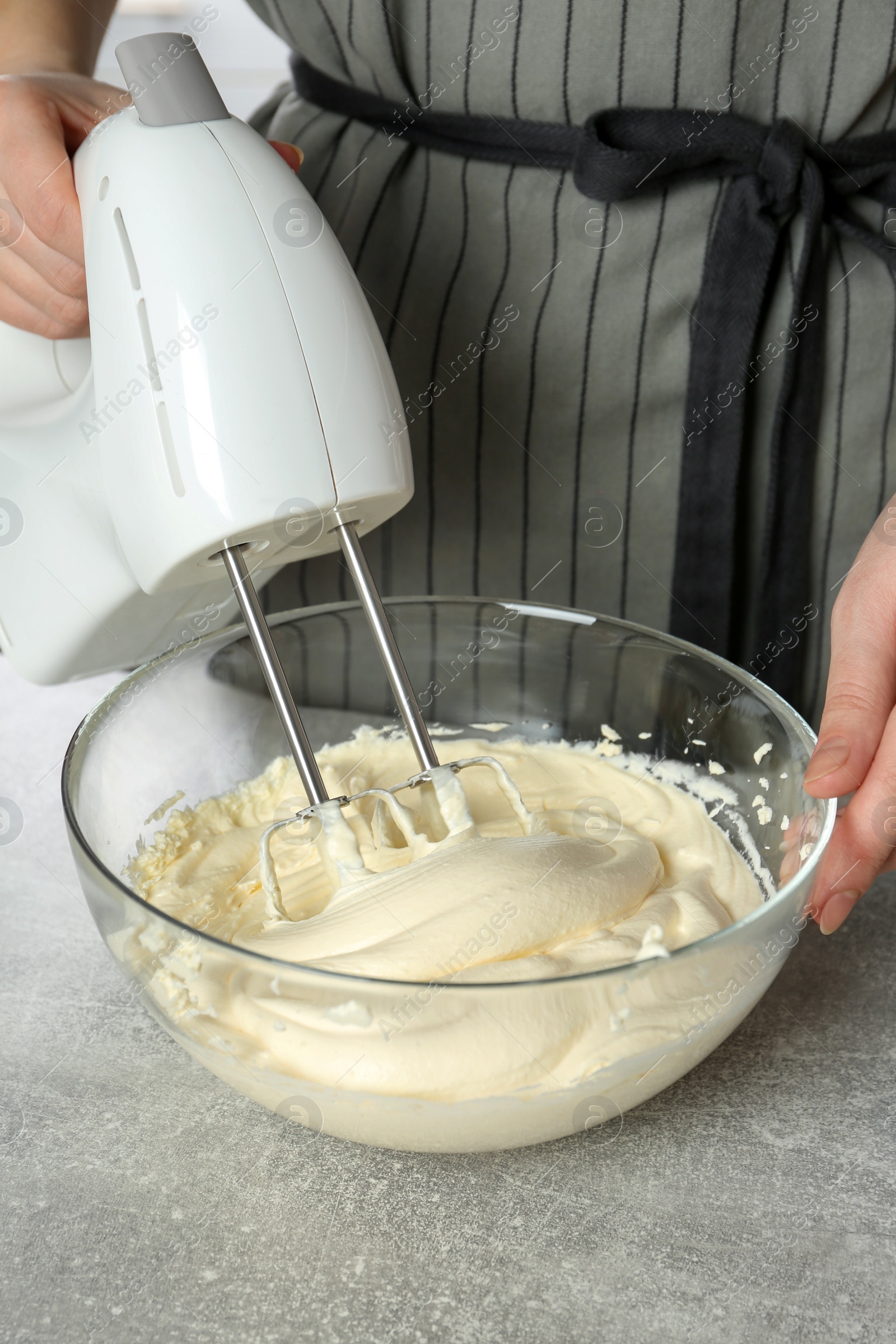 Photo of Woman whipping white cream with mixer at light grey table, closeup