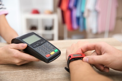 Man using terminal for contactless payment with smart watch in shop, closeup