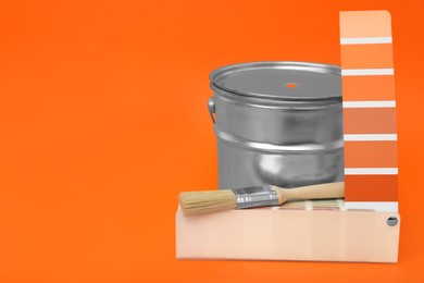 Photo of Can of paint, brush and color palette samples on orange background. Space for text