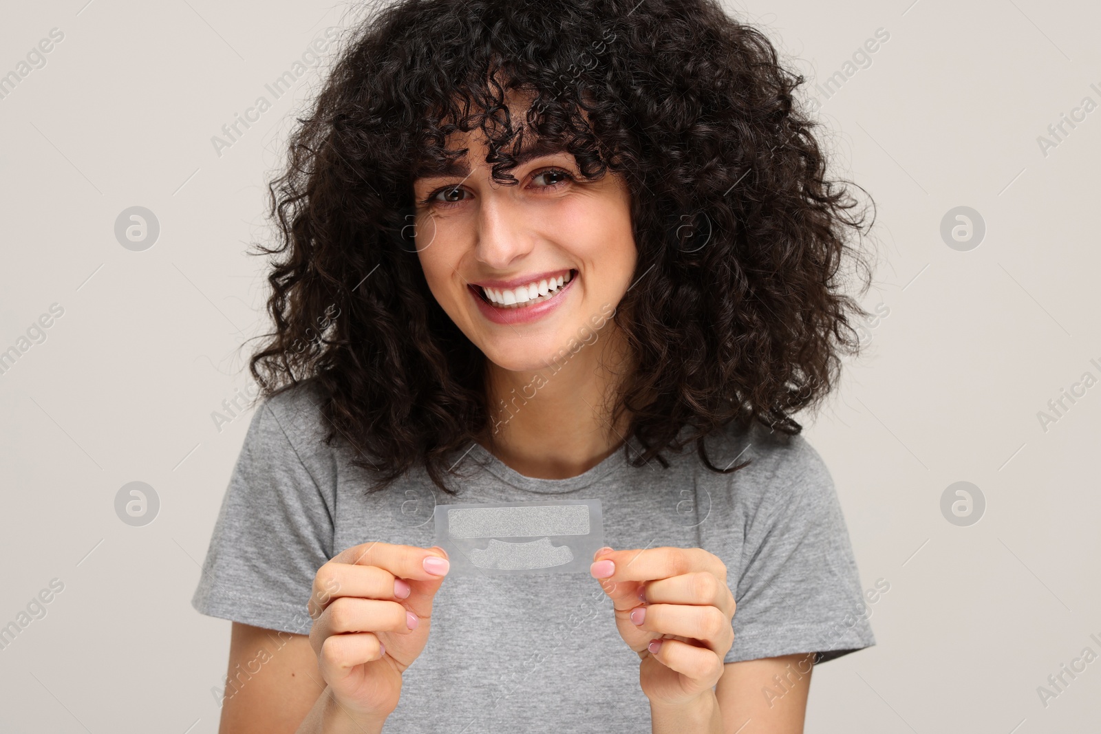 Photo of Young woman holding teeth whitening strips on light grey background