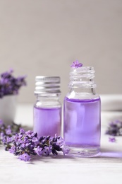 Glass bottles of natural cosmetic oil and lavender flowers on white wooden table