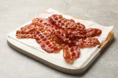 Photo of Board with fried bacon slices on grey textured table, closeup