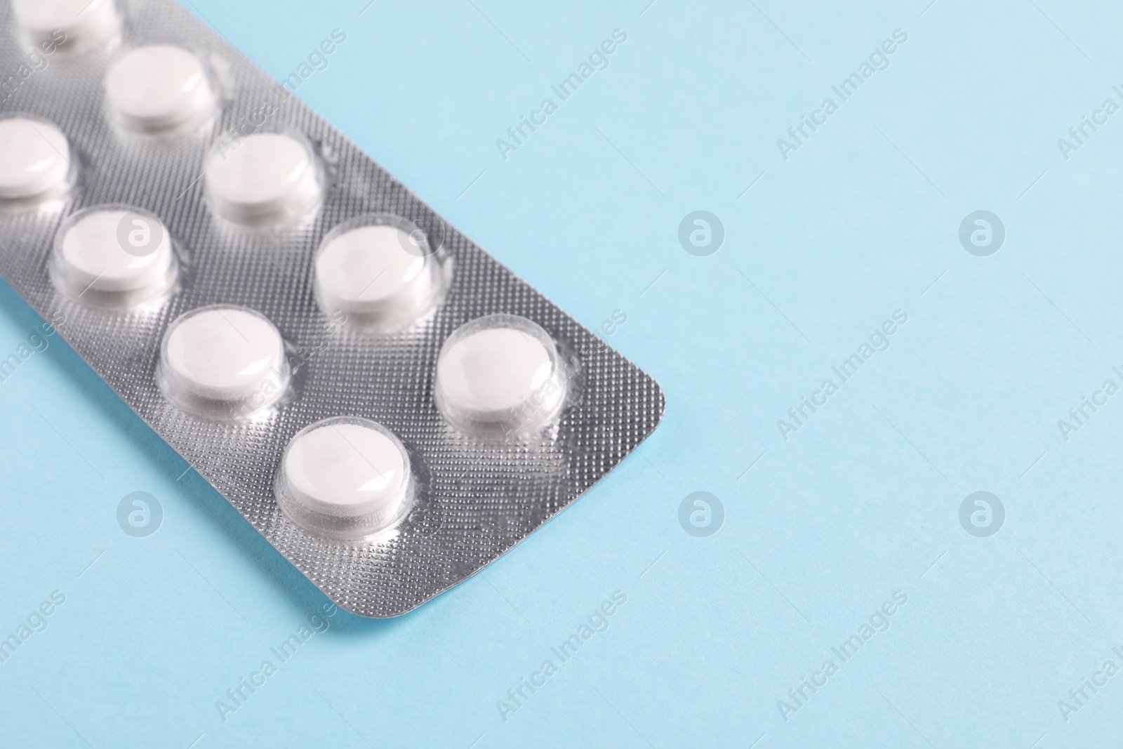 Photo of White pills in blister on light blue background, closeup. Space for text