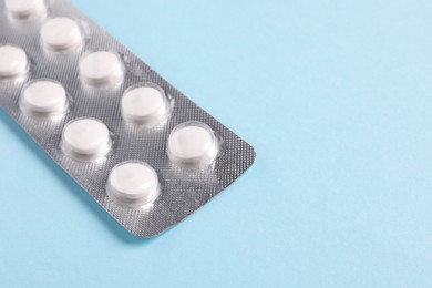 Photo of White pills in blister on light blue background, closeup. Space for text