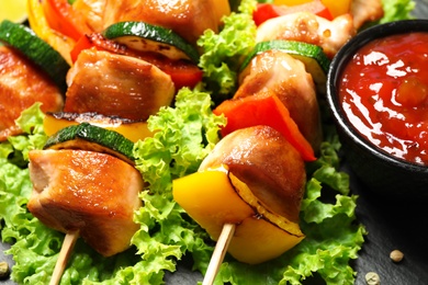 Photo of Delicious chicken shish kebabs with vegetables on slate plate, closeup
