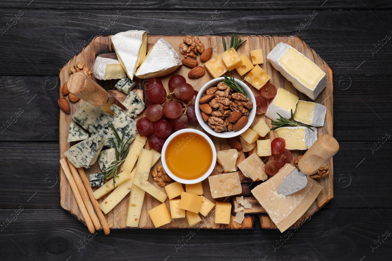 Photo of Cheese plate with honey, grapes and nuts on black wooden table, top view