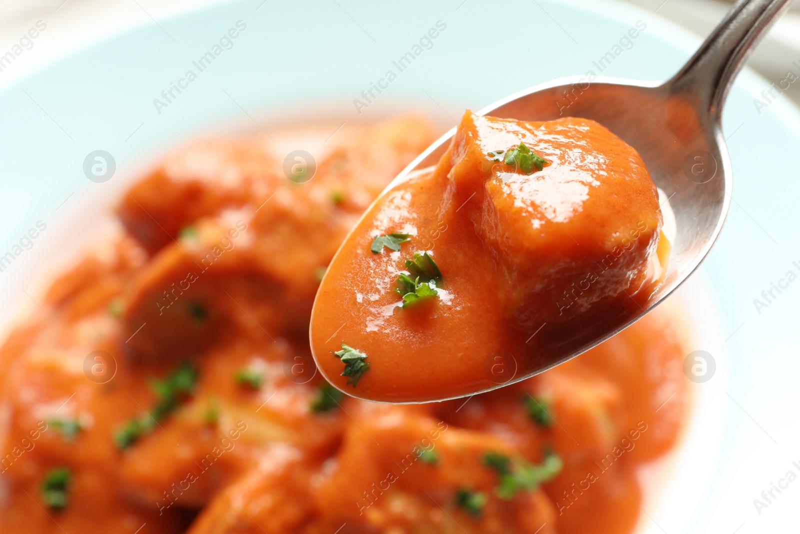 Photo of Tasty butter chicken in spoon over plate with meal. Traditional Murgh Makhani dish