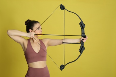 Woman with bow and arrow practicing archery on yellow background