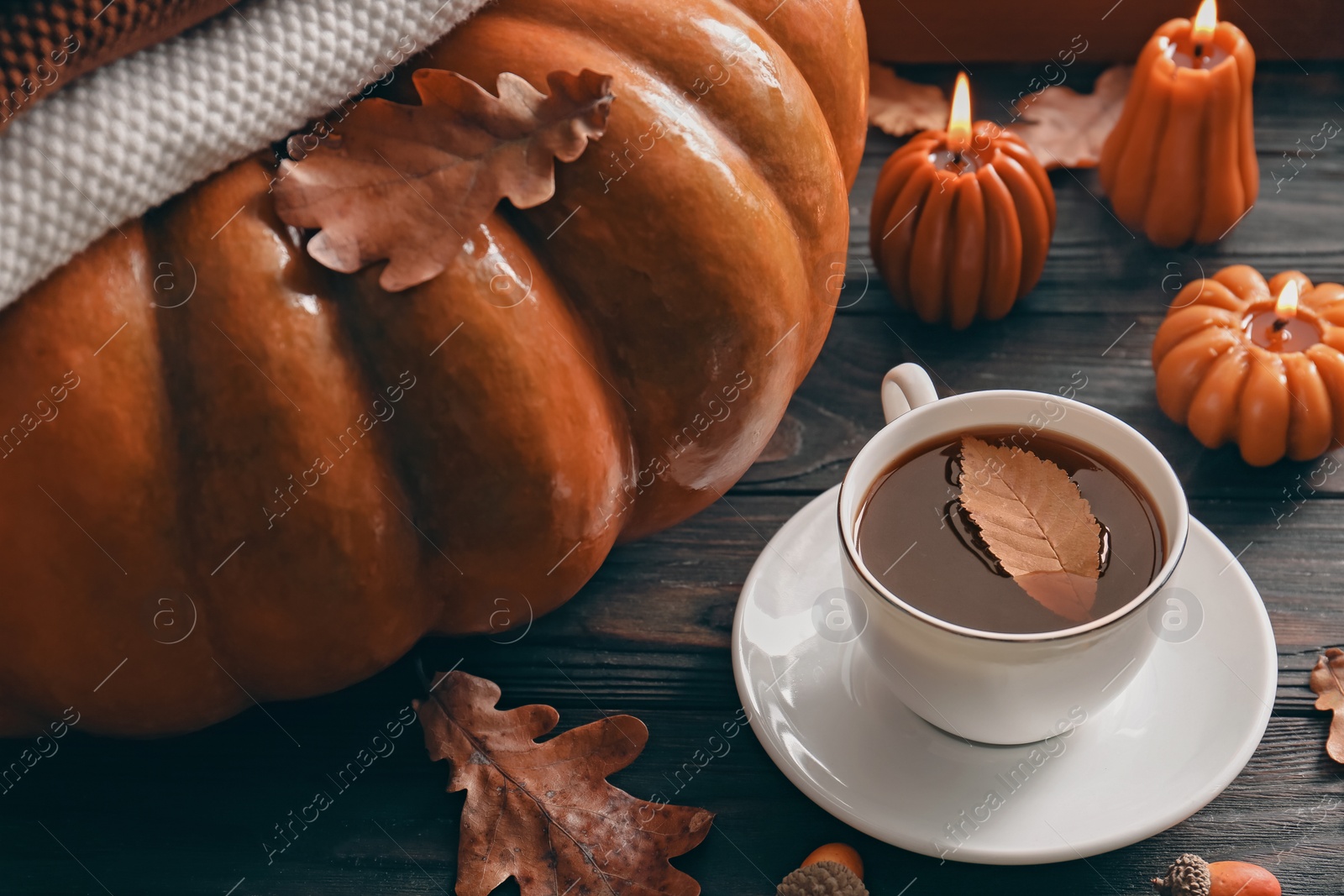 Photo of Cup of hot drink and pumpkin shaped candles on wooden table. Cozy autumn atmosphere