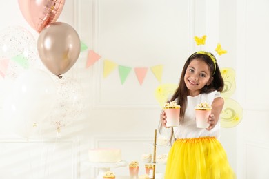 Photo of Cute little girl wearing fairy costume with popcorn in decorated room. Space for text
