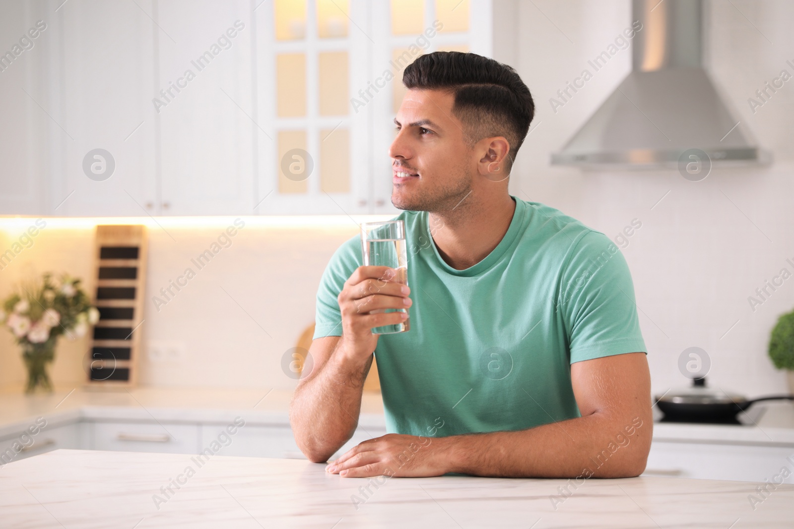 Photo of Man holding glass of pure water at table in kitchen