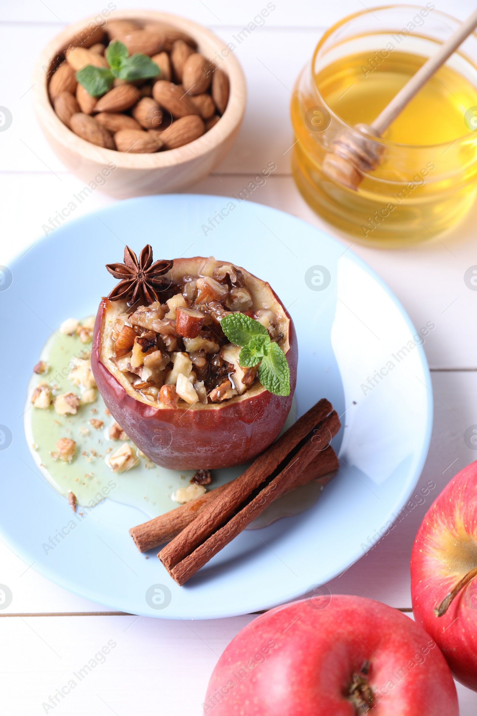 Photo of Tasty baked apple with nuts, honey, spices and mint on white wooden table, above view