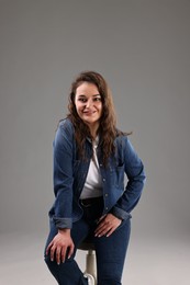Photo of Portrait of beautiful young woman sitting on chair against grey background