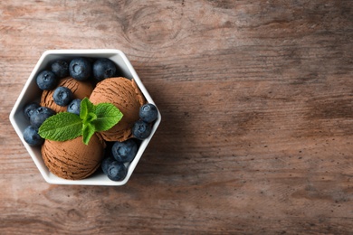 Bowl of chocolate ice cream and blueberries on wooden table, top view. Space for text