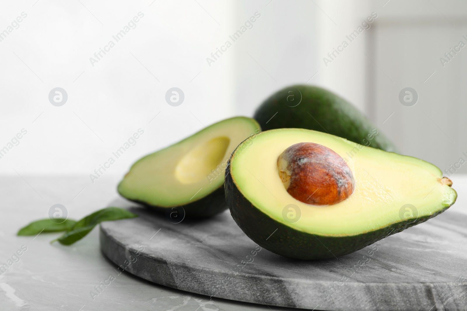 Photo of Halves of delicious ripe avocado on table against light background