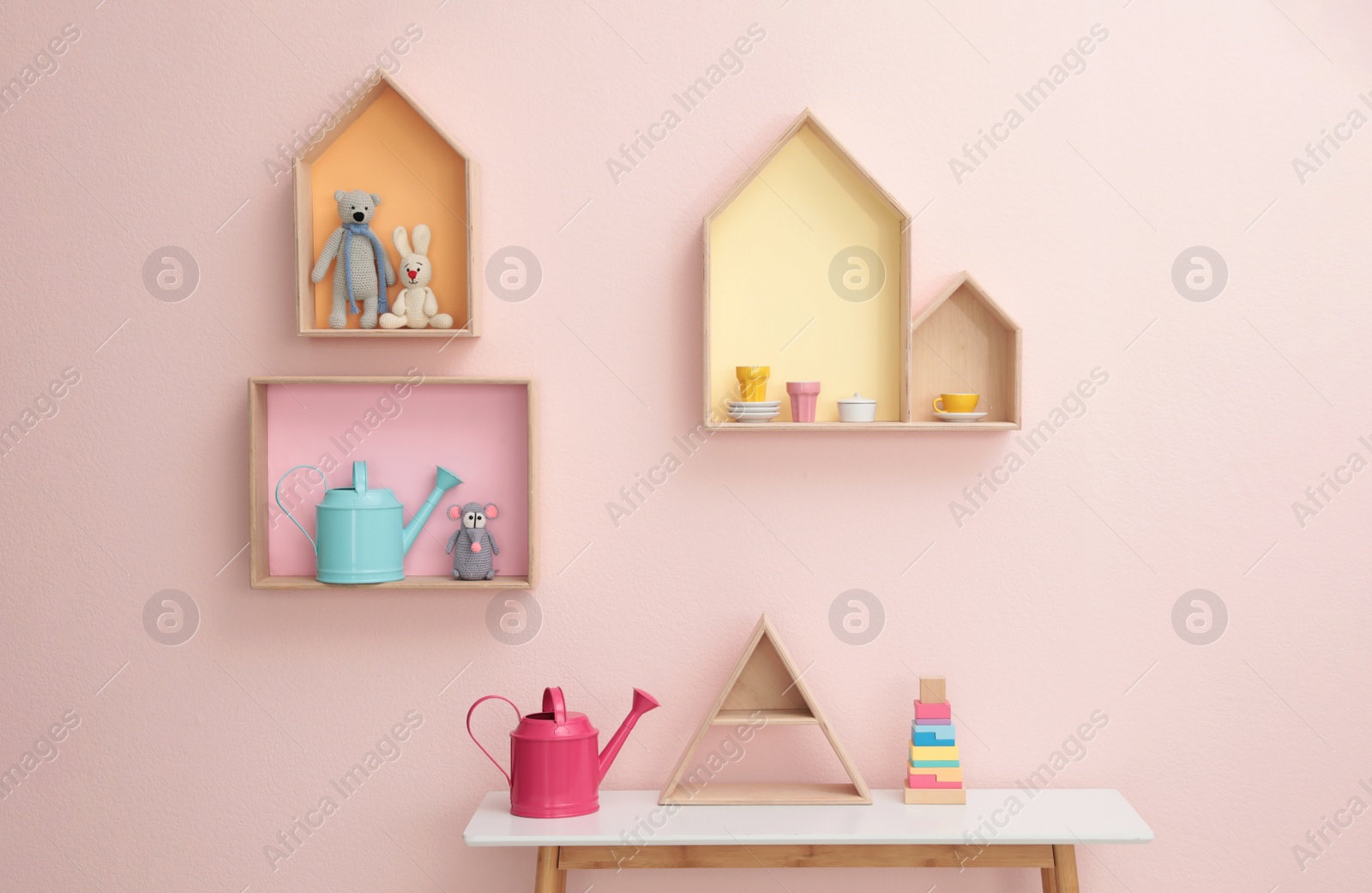 Photo of Stylish house shaped shelves with toys and wooden table indoors. Baby room interior design